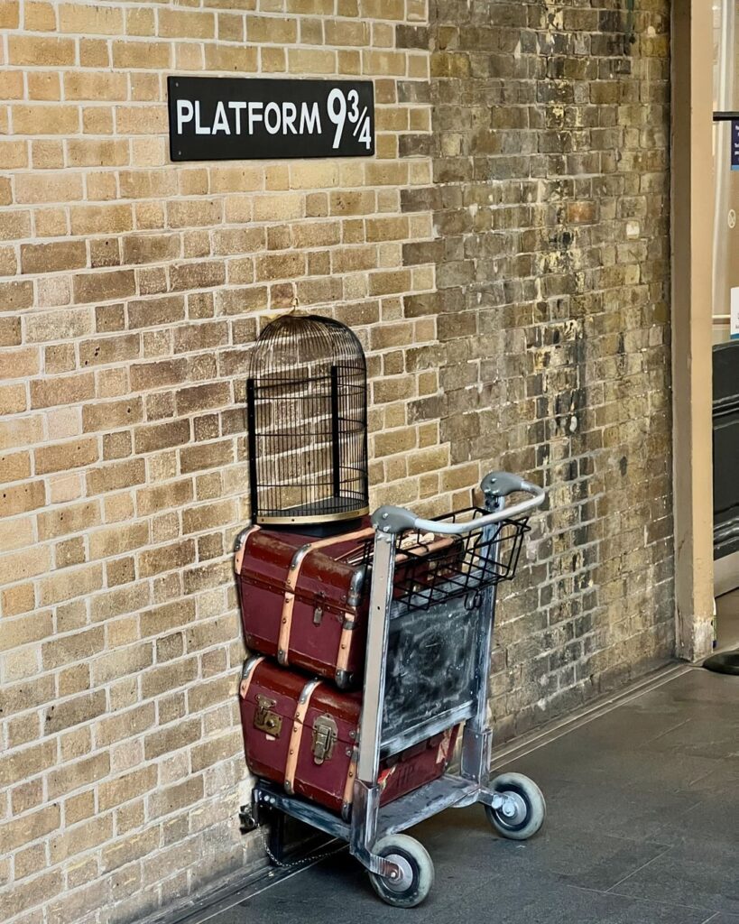 The iconic Platform 9 ¾ setup at King's Cross Station in London, featuring a luggage trolley appearing to disappear into the wall.