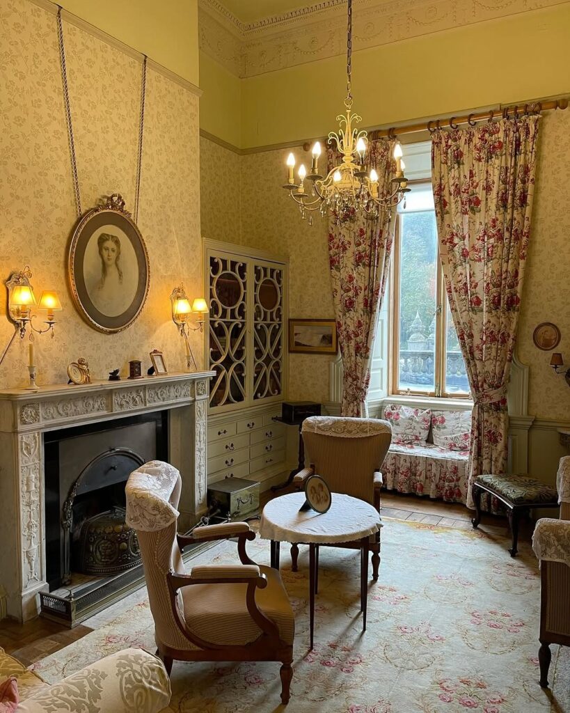 Elegant interior of Westport House, featuring vintage furniture, a decorative fireplace, floral curtains, and a chandelier, showcasing timeless Georgian charm