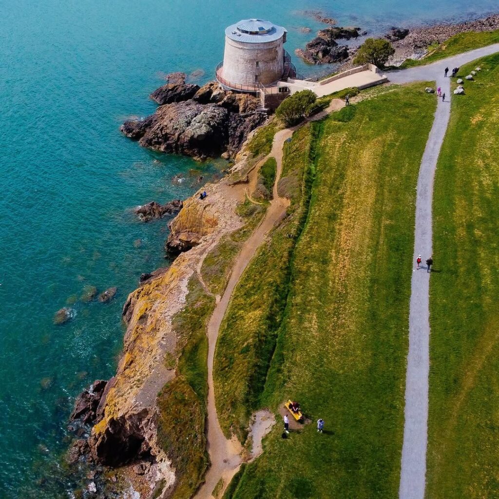 Martello Tower in Dublin Bay, overlooking the calm waters and rocky shoreline, with a scenic coastal path under a cloudy sky
