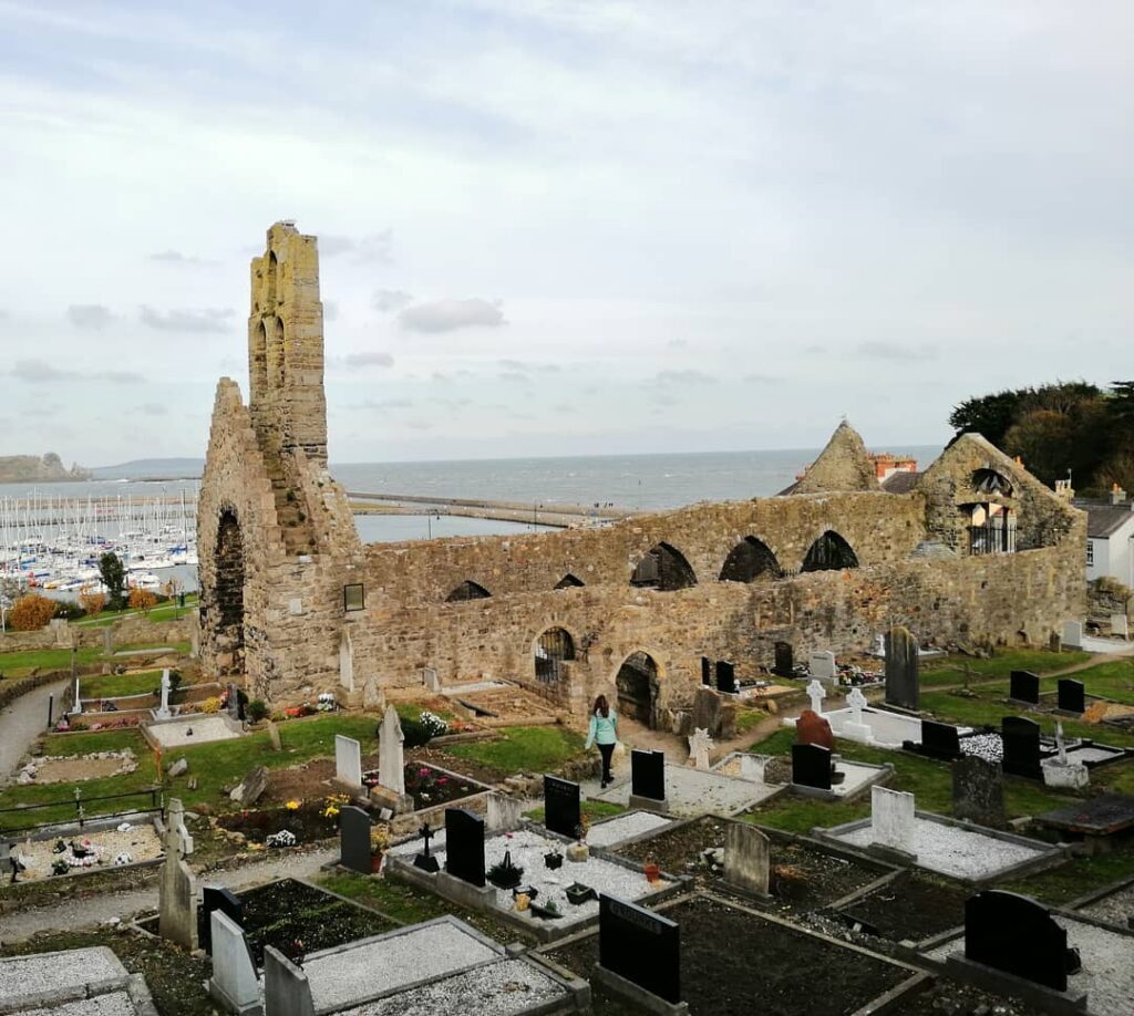 St. Mary’s Abbey, Howth, showcasing the historic ruins with a serene graveyard, overlooking the marina and the Irish Sea under a cloudy sky