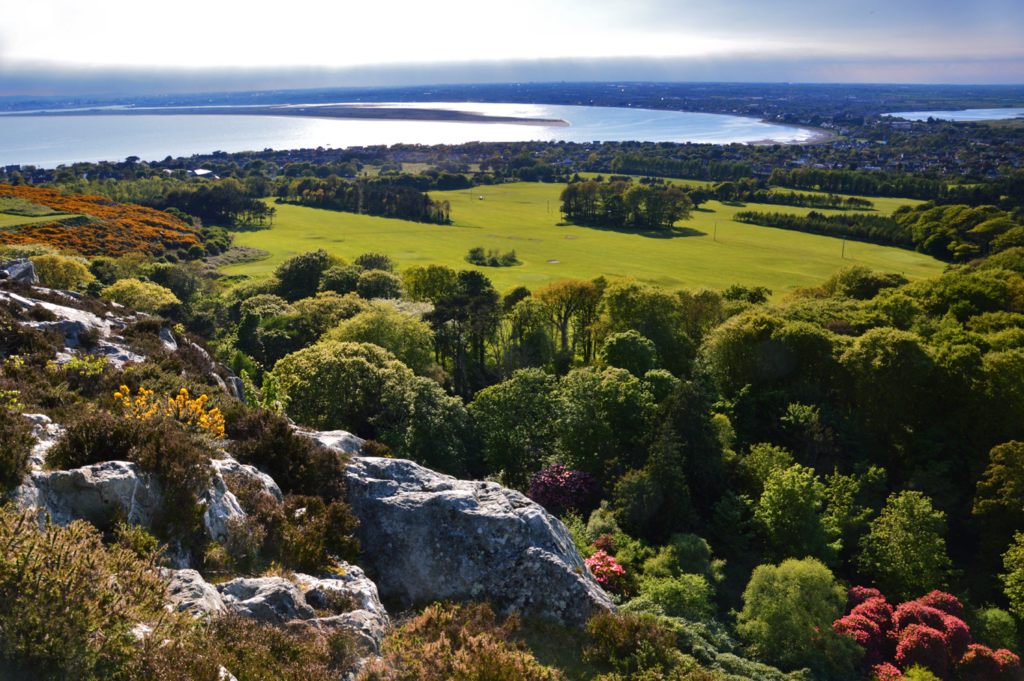 Scenic view of Deer Park, Howth, featuring lush greenery, rocky terrain, and panoramic views of Dublin Bay under a bright, clear sky