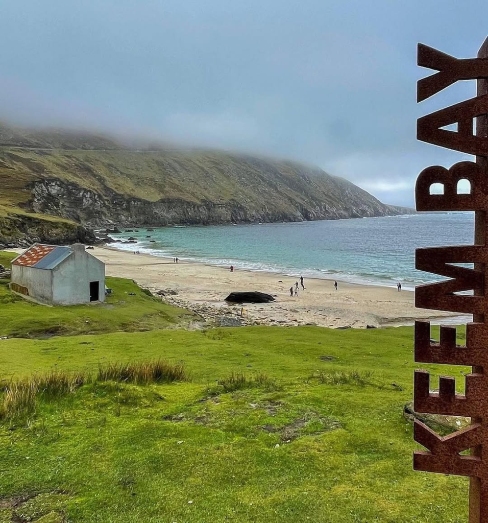 Keem Bay, a stunning Achill Island beach with soft golden sand, turquoise waters, and dramatic cliffs shrouded in mist, offering a serene and picturesque escape