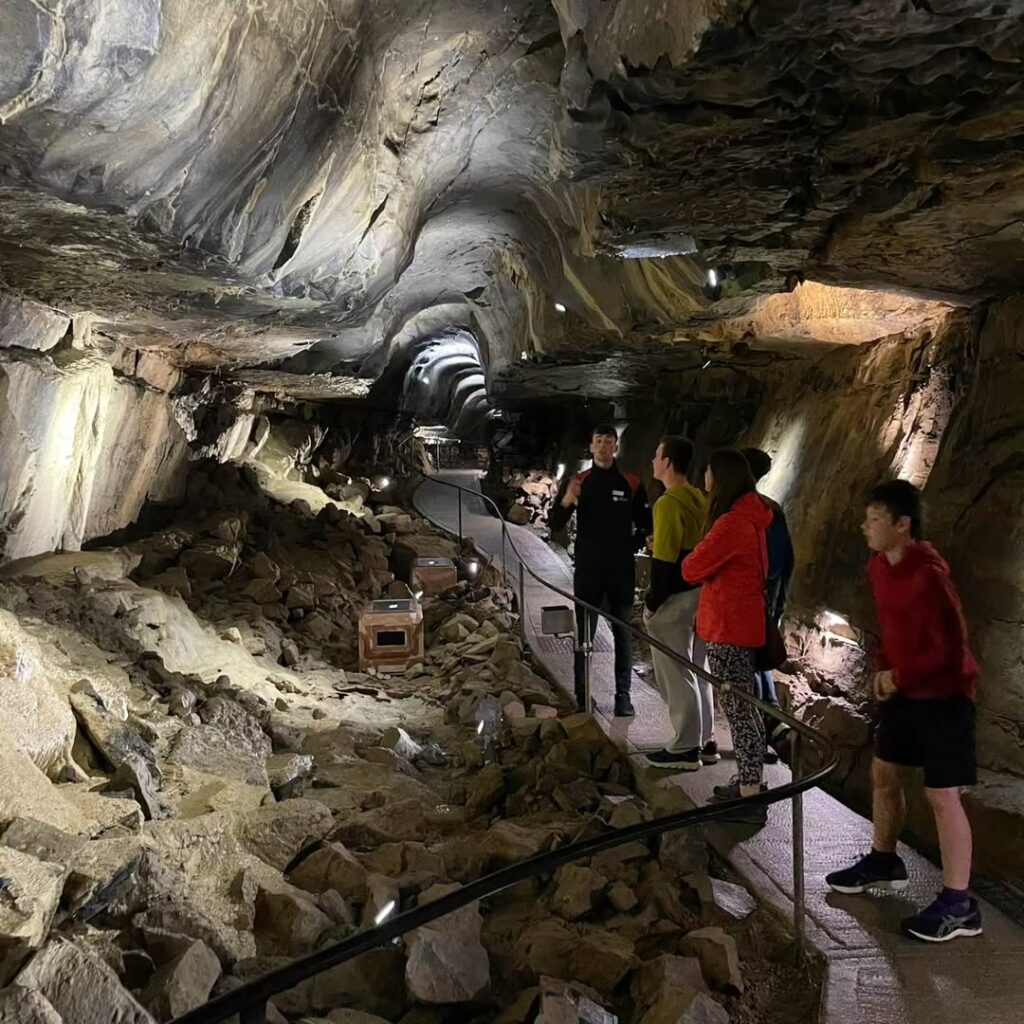 A group of people touring inside Aillwee cave with rugged rock formations, guided by an expert who is explaining the site.