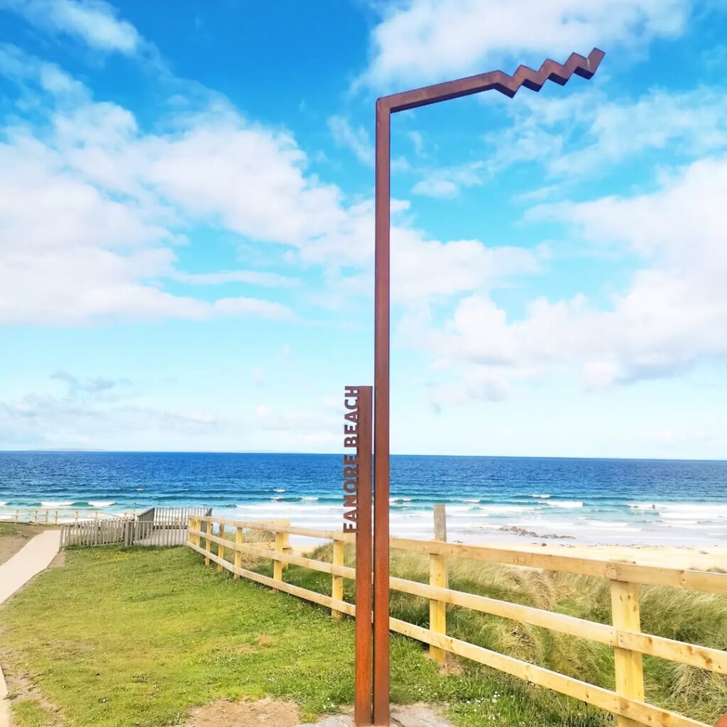 The distinctive sign for Fanore Beach, standing against a backdrop of the beach and the Atlantic Ocean with bright blue skies.