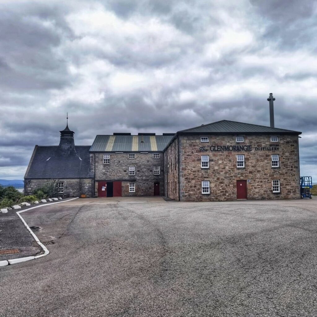 Glenmorangie Distillery, a historic whisky distillery, with stone buildings and a cloudy sky.