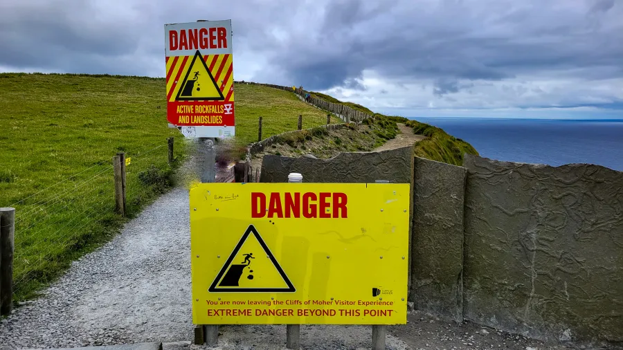 Warning signs at the Cliffs of Moher indicating extreme danger beyond the point, cautioning visitors about rockfalls and dangerous landscapes.