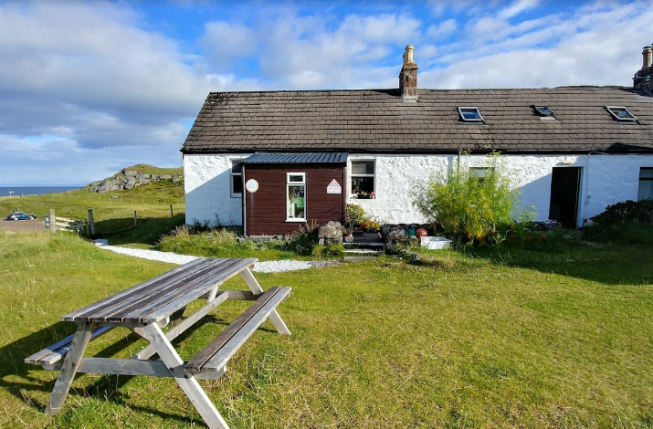 Quaint white bothy with a picnic table and lush green surroundings, offering a rustic retreat.