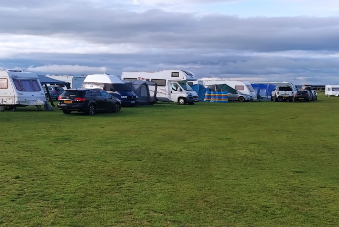 Dornoch Camping site with motorhomes, caravans, and tents on a grassy field along the North Coast 500 Scotland under a cloudy sky