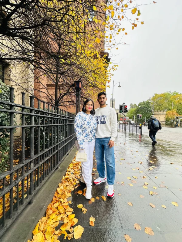 Yashvi and Meet, creators of Budget Wanderers, posing on a vibrant autumn day in Edinburgh, surrounded by golden leaves and the cityâs historic charm