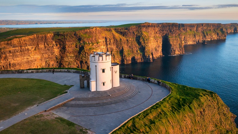 Aerial view of O'Brien's Tower at the Cliffs of Moher, with the dramatic cliffs and Atlantic Ocean in the background during golden hour.