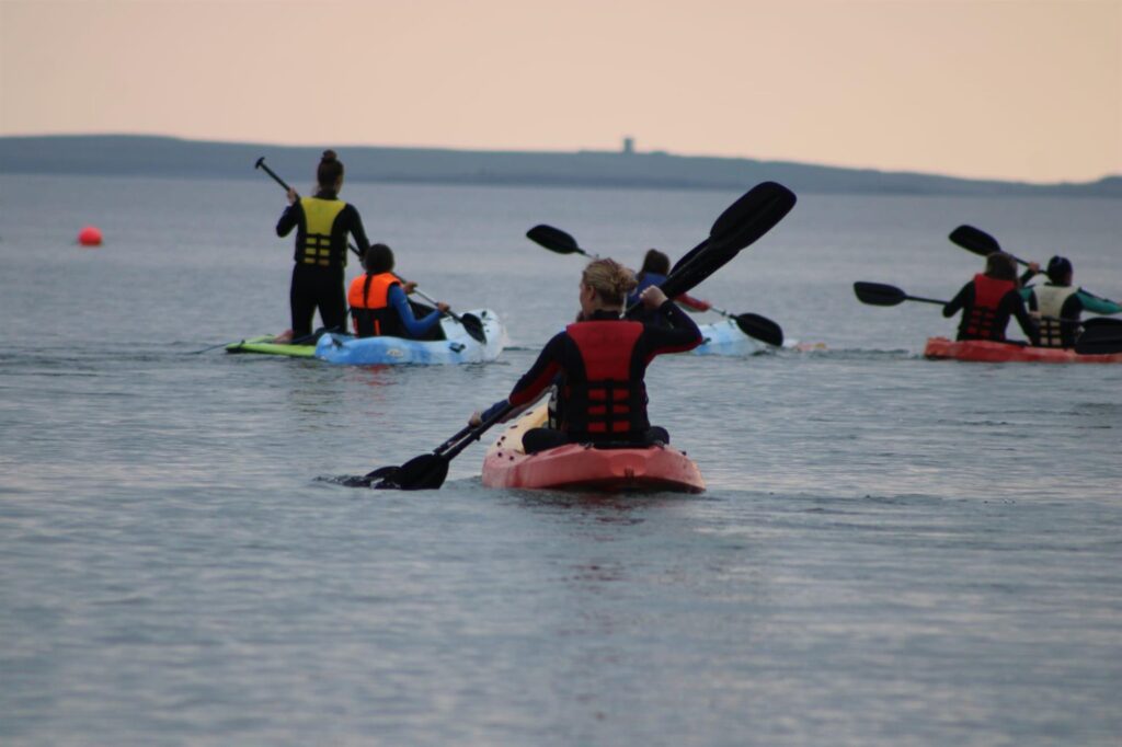 A group of people kayaking on calm waters near the Cliffs of Moher, wearing life jackets and paddling along in different colored kayaks