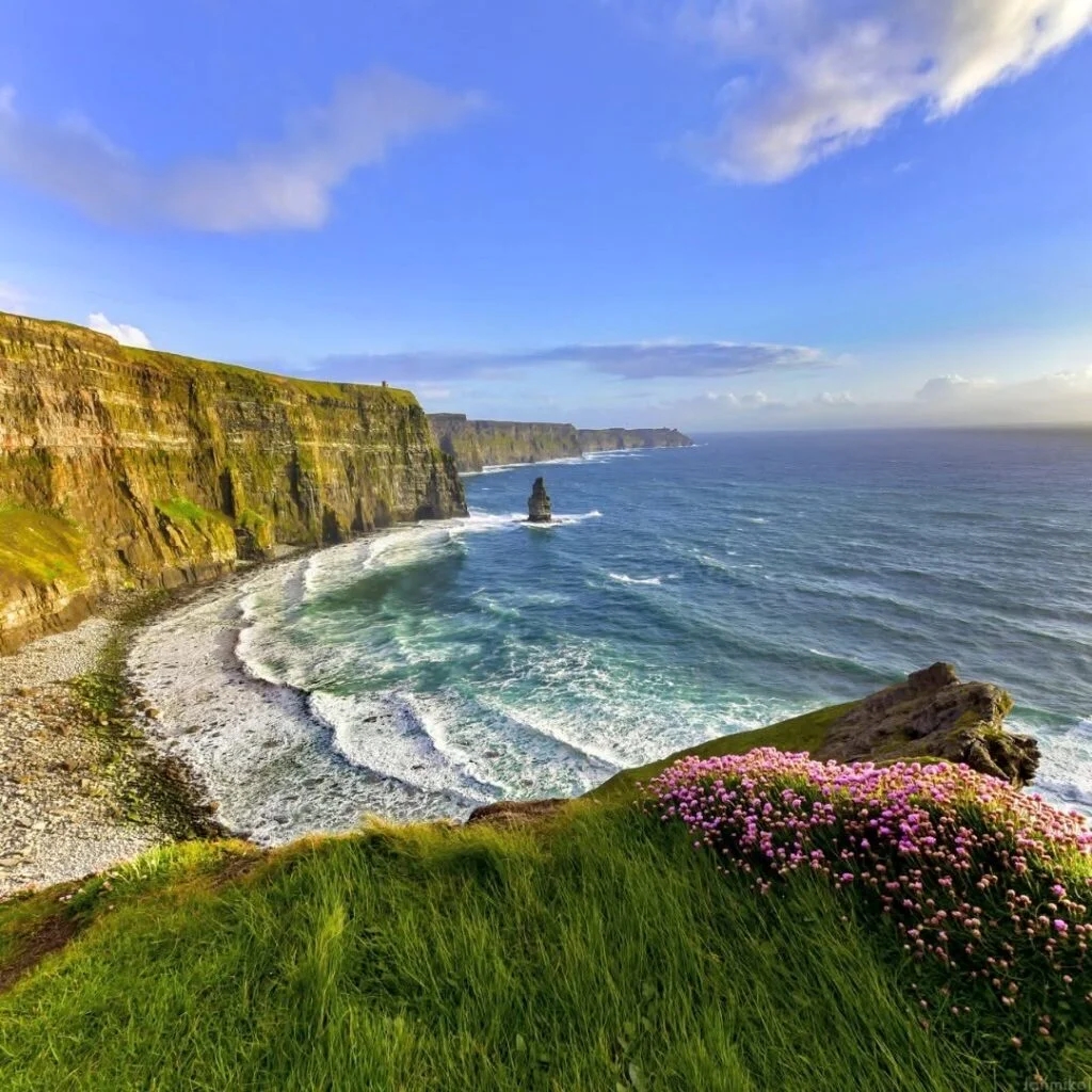 A breathtaking view of the Cliffs of Moher, showing the rugged coastline, towering cliffs, and the Atlantic Ocean with waves crashing against the shore.