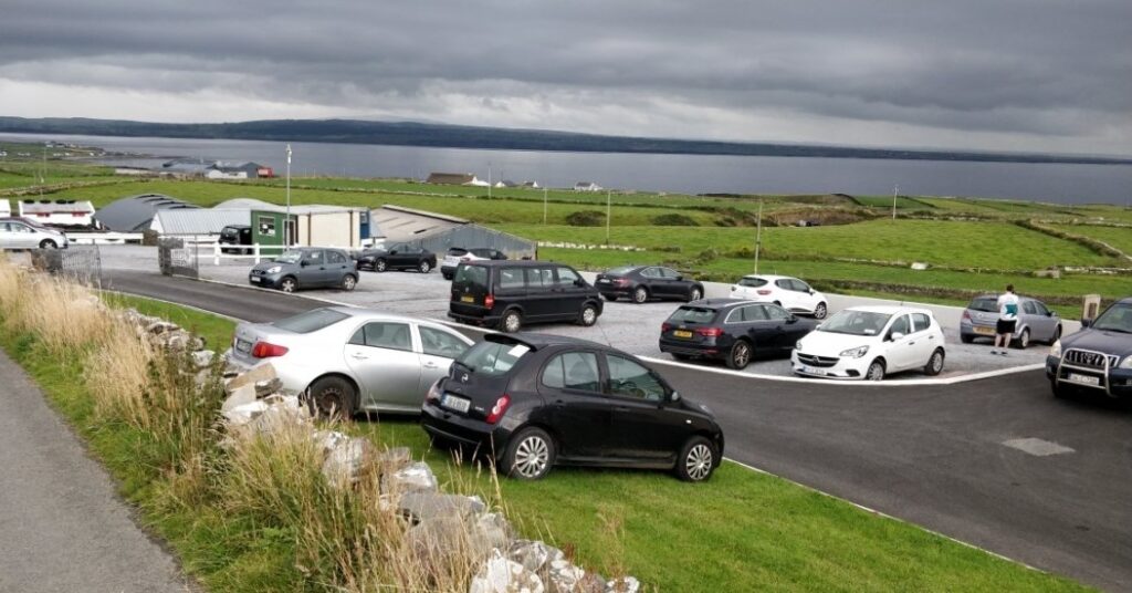 The parking lot near the Cliffs of Moher, with cars parked and the green Irish landscape in the background, leading towards the Atlantic coast.