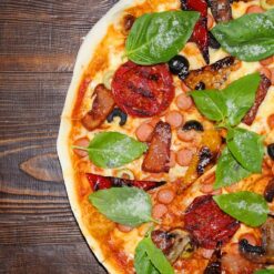 Close-up of a delicious pizza with toppings including fresh basil, tomatoes, sausages, olives, and mushrooms, perfect for pizza lovers seeking tasty, affordable meals.