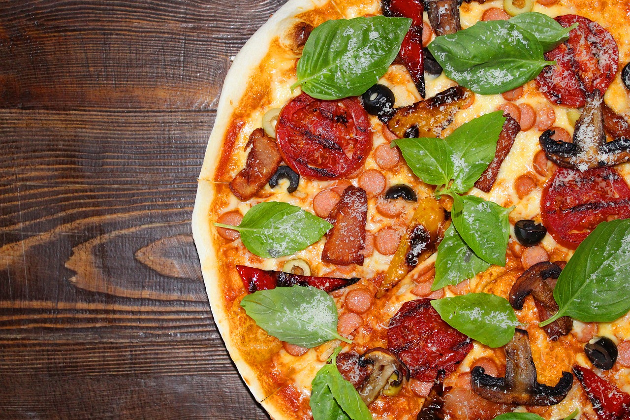 Close-up of a delicious pizza with toppings including fresh basil, tomatoes, sausages, olives, and mushrooms, perfect for pizza lovers seeking tasty, affordable meals.