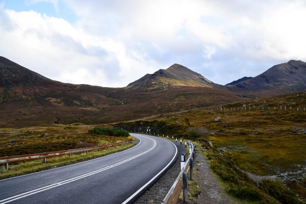 Winding road through the rugged landscape of the Scottish Highlands on the North Coast 500 Scotland, with hills and moorland under a partly cloudy sky.