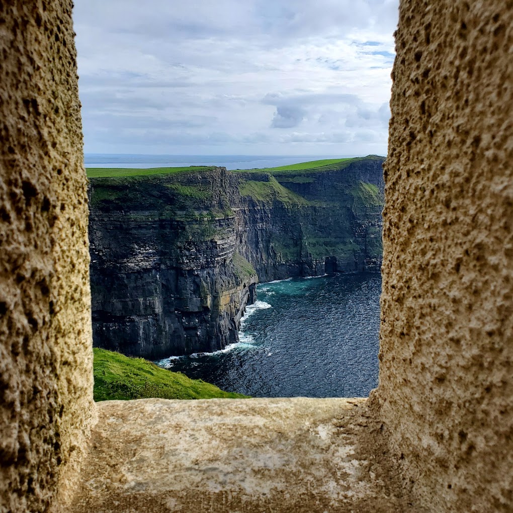 A view of the Cliffs of Moher from the window of O'Brien's Tower, showcasing the rugged cliffs and the Atlantic Ocean below, framed by the stone window.