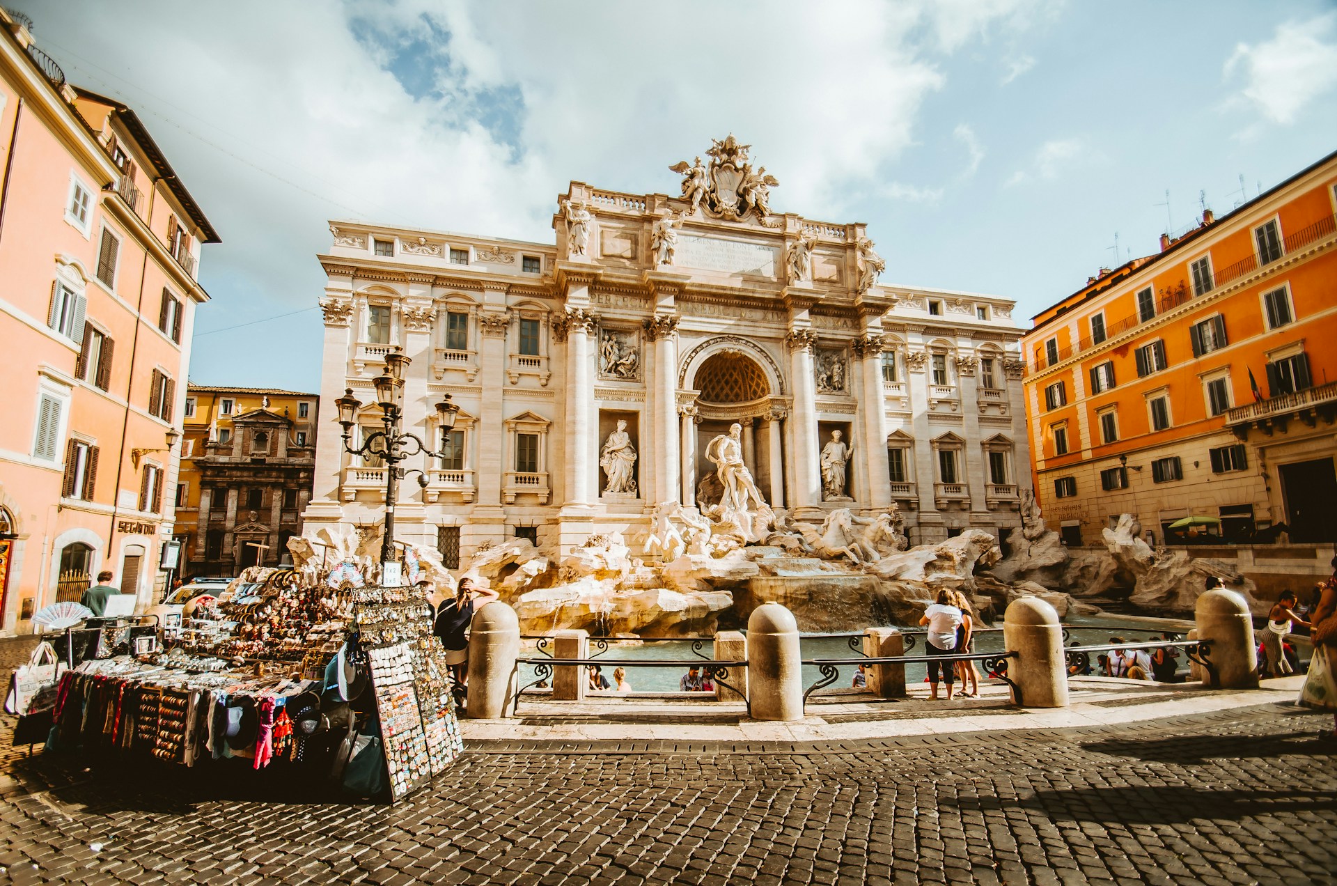 The Trevi Fountain in Rome, Italy, with its grand Baroque architecture, cascading water, and statues of Oceanus and Tritons, surrounded by historic buildings and a street market in the foreground.